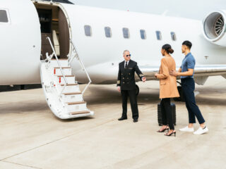 Passengers boarding in private luxury jet near hangar, pilot welcomes the young successful passengers - Sharon Carr Travel