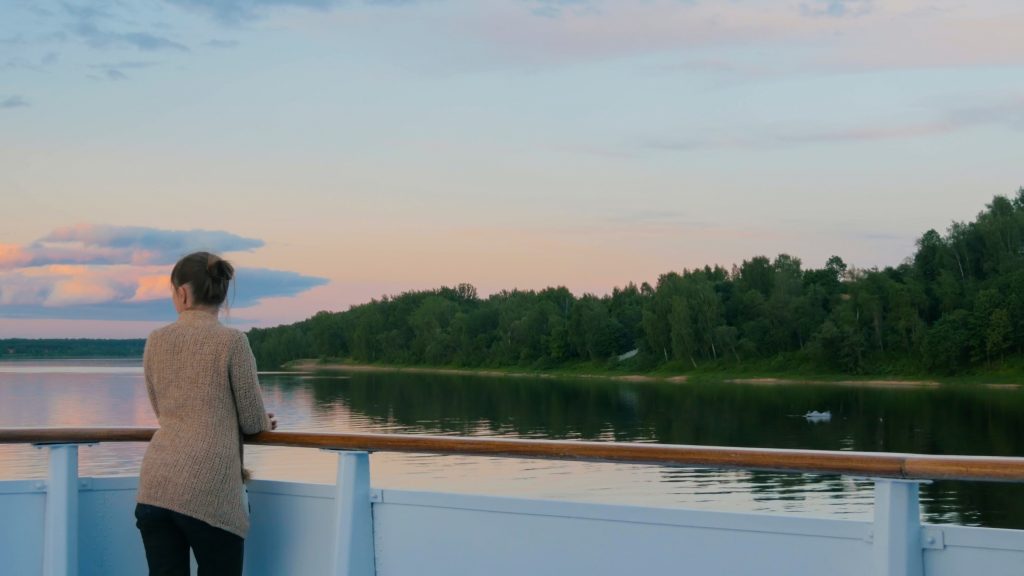 Woman standing on deck of cruise ship and looking at landscape - Sharon Carr Travel