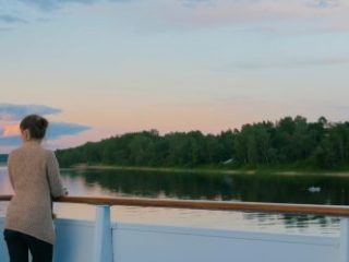 Woman standing on deck of cruise ship and looking at landscape - Sharon Carr Travel